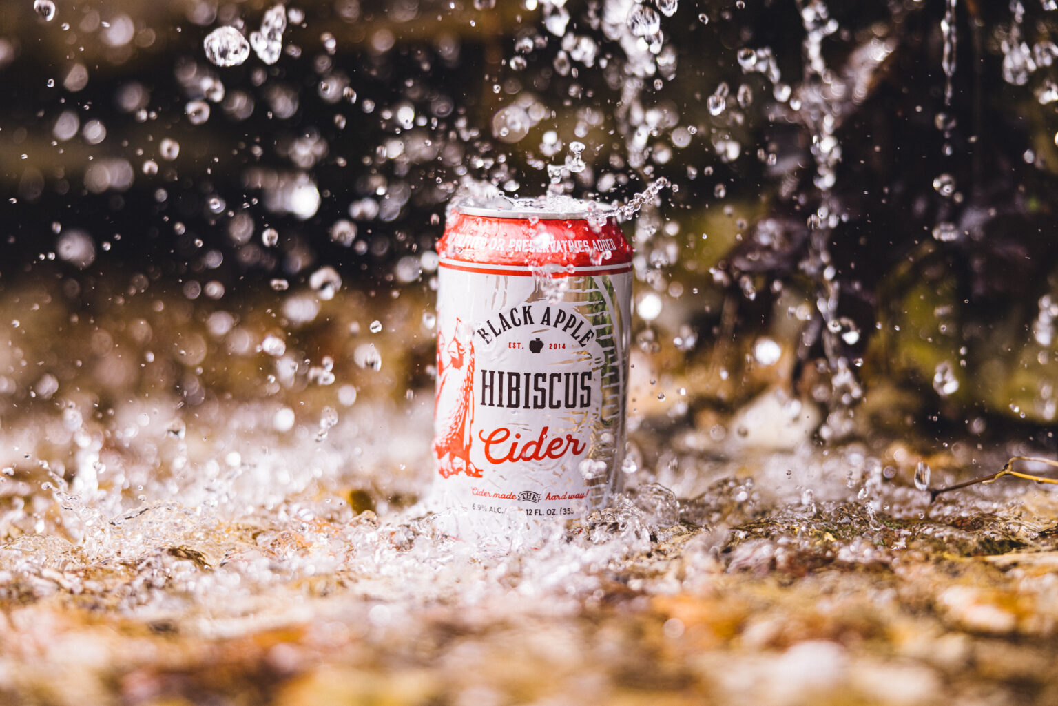 A can of Black Apple Hibiscus cider sitting in a creek with water splashing around it.